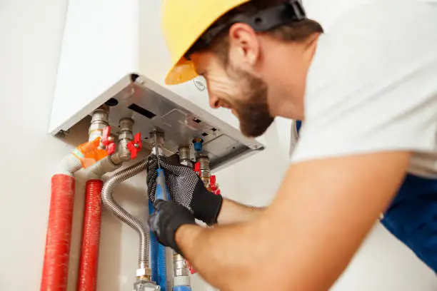 Photo of Closeup of plumber using screwdriver while fixing boiler or water heater, working on heating system in apartment