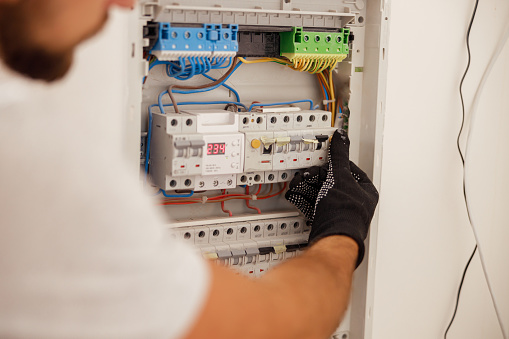 Hand of electrical technician working with fuses at the circuit breaker control cabinet on the wall. Manual work, maintenance, repair service concept