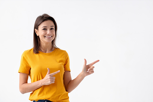 Beautiful Caucasian young woman smiling with his finger pointing on a white background with copy space, looking at the camera and smiles friendly
