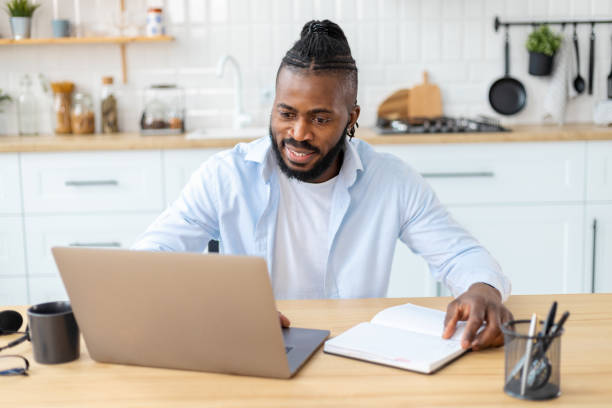 istock Portrait of smiling African American confident businessman using laptop computer taking notes working from home. Remote work concept 1391881746