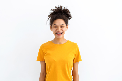 Portrait young funny positive smiling African American woman dressed in yellow t shirt on white background, good mood concept