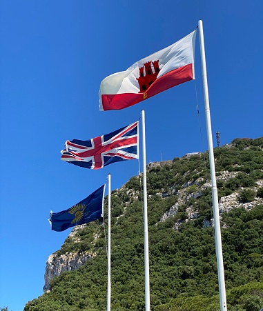 Three flags flying in front of the rock of Gibraltar, the flag of Gibraltar, the British flag and the flag representing the Commonwealth
