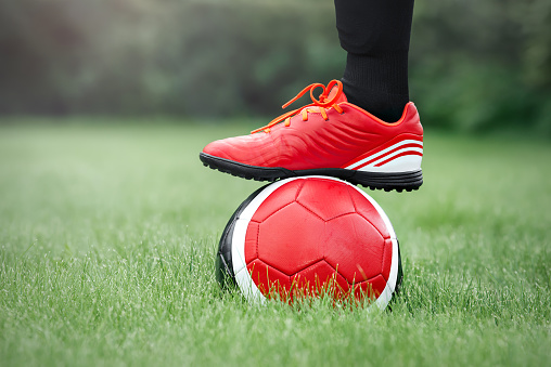 Football training. Beautiful red soccer ball and foot in red artificial turf boots.