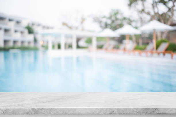 istock Empty white marble stone table top and blurred swimming pool in tropical resort in summer banner background - can used for display or montage your products. 1391897314