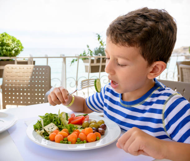 Child is happy because he must to eat vegetables. There is a lot of vegetables on his plate