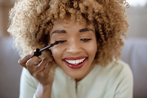 Beautiful african american woman applying mascara with brush, using decorative makeup