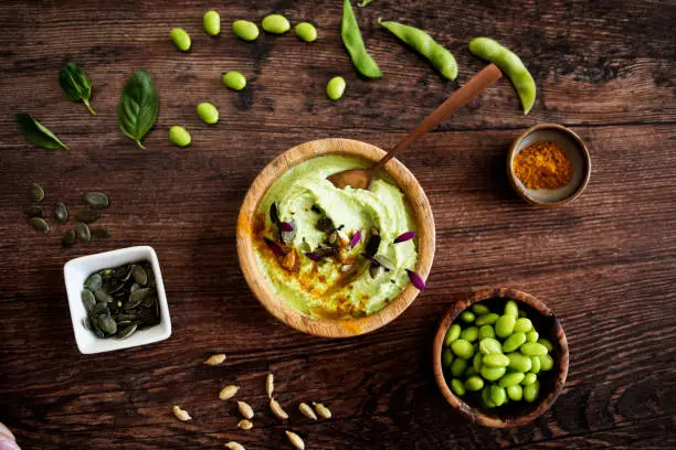 bowl of guacamole with pumpkin and edamame seeds, soy pods and paprika on a wooden table