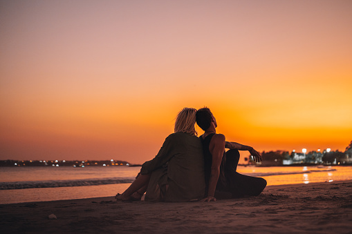 Rear view of a young couple enjoying on the beach in a dramatic orange- red -yellow sunset