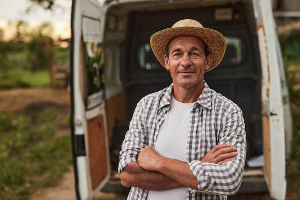 Farmer standing near delivery trunk Smiling mature male farmer in straw hat standing with crossed arms against blurred van prepared for delivery of products at local market farmer stock pictures, royalty-free photos & images