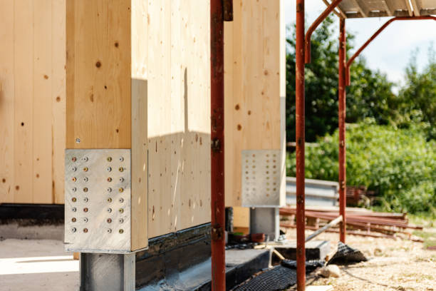 Wooden wall anchored to base by steel post bases. Sunny day. Construction site, building modern family house.