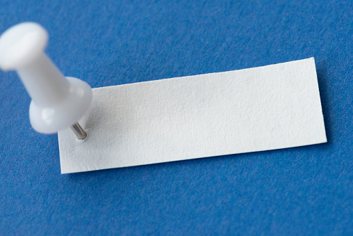 Small white paper pinned with a white pin on blue background.
