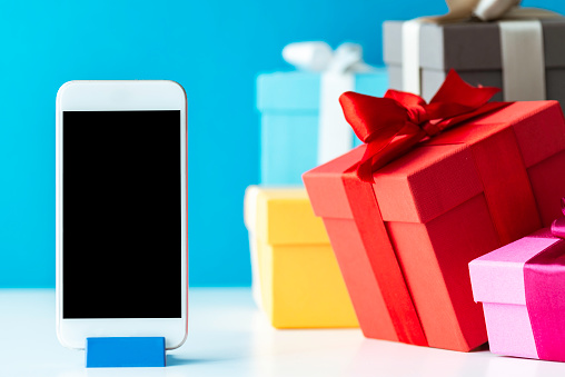 Multicolored gift boxes and a smart phone on white table in front of a blue wall.