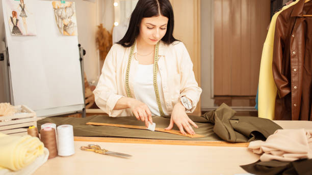 istock black haired seamstress in atelier, portrait at work. Table with fabric and sewing tools, indoors. draws with soap and ruler 1391910173
