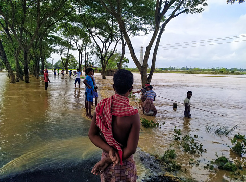 Katwa WB India - October 3, 2021 : Taken this picture during the flood in West Bengal where villagers are crossing the inundated countryside on boat. Few people are fishing and few crossing the street carrying belongings. The three vilalgers on the boat fishing