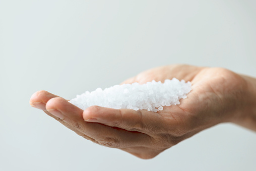 Hand is holding salt crystals to camera in front of white background.