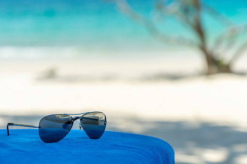 Sunglasses on beach chair with crystal sea and white sand background