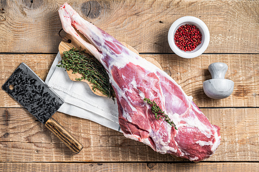 Butcher board with  Raw lamb mutton leg with herbs. Wooden background. Top view.