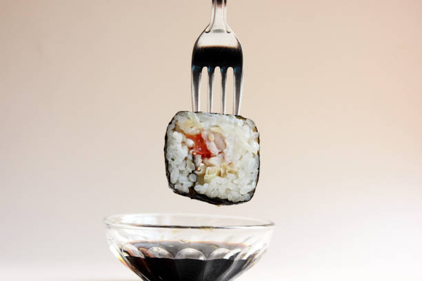 Fresh sushi roll on a fork in the middle, isolated on a light background. Soy. How to eat sushi without sticks. Asian cuisine. Copy space. Close-up.