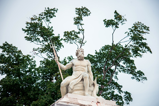 statue of ancient god Neptune with trident on tree background with green leaves. Patron of horses and chariot races. A god of moisture, of the sea, and a protector of drought.