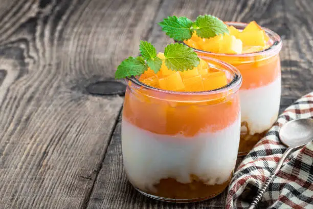 Photo of White fruity yogurt in glass jars on wooden table