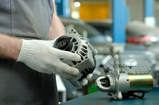 The car generator is in the hands of an auto mechanic. There is a car starter on the desktop. Repair and maintenance of the car in the service center.