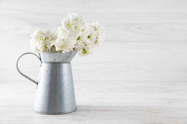White flowers in a vase on rustic wooden table. Blank space for text on the wall