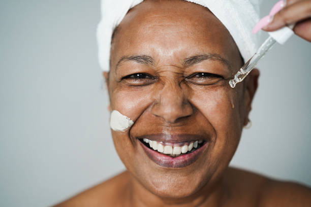 mujer africana mayor que se aplica un tratamiento de belleza de gota hialurónica y máscara para la piel en su cara - focus on eyes - wrinkled women mature adult beauty fotografías e imágenes de stock