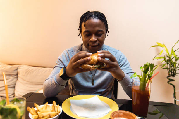 istock Young African American man enjoying eating burger and drinking cocktail 1391931083