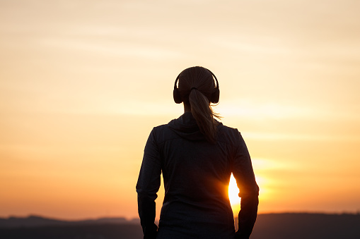 Woman with headphones listening music during sunset. Silhouette of female person at dusk. Relaxation outdoors