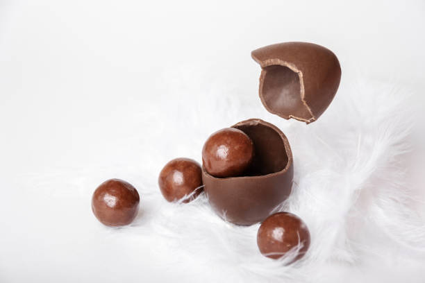 istock Cracked chocolate easter egg with chocolate small round candies and flying eggshell in white feather nest 1391932361