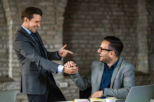 Two happy entrepreneurs celebrating their success in office and giving each other high-five.