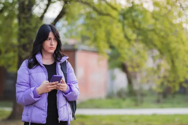 Photo of Girl holding smart phone when standing in the park