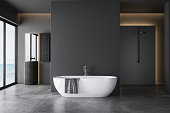 Dark grey bathroom with white bathtub and two sinks with square mirrors and shower area.