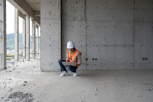 A male engineer works on a laptop at a construction site for a modern office building.