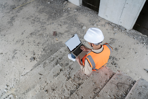 A male engineer works on a laptop at a construction site for a modern office building.