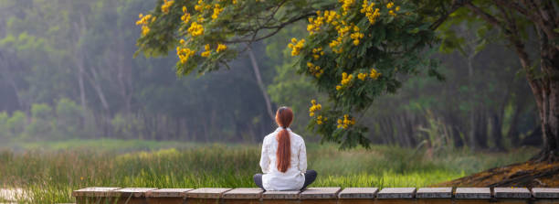 vista panorámica de la mujer practicando relajantemente la meditación en el parque público para alcanzar la felicidad de la sabiduría de la paz interior con flores amarillas en verano - conciencia plena fotografías e imágenes de stock