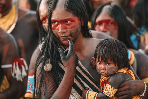 Indigenous mother holding baby Indigenous woman with half-shaved head, from an Amazon tribe in Brazil, holding her baby, with their bodies and faces covered in red and black paint. Jogos Indígenas 2009. indigenous peoples day stock pictures, royalty-free photos & images