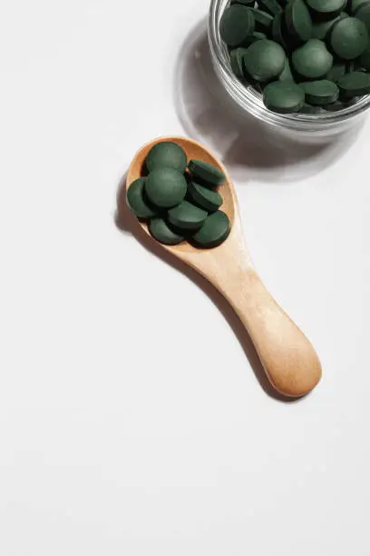 Photo of natural additives and superfood. green spirulina algae pills in spoon and glass bowl on white background. healthy concept.organic food copy space