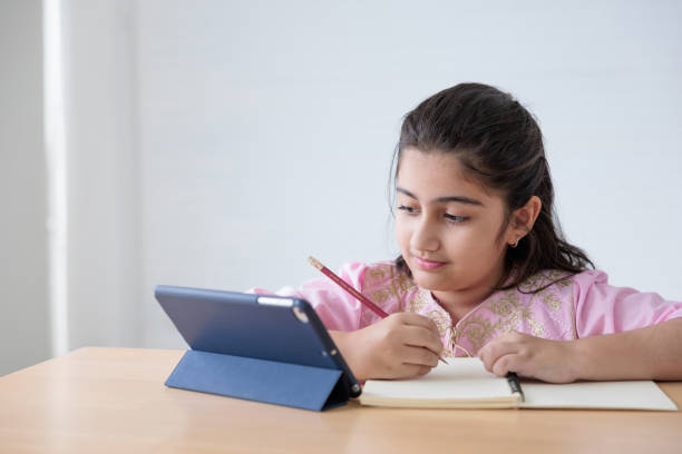 istock cute Indian girl writing on notebook and looking tablet for online learning class, education concept 1391963260