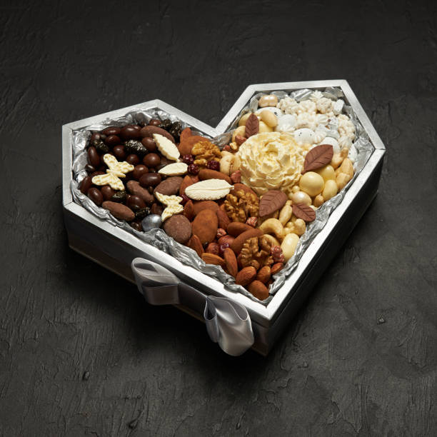 Heart shaped box filled with chocolate candies and nuts on a black background stock photo