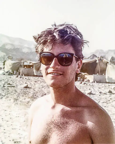 Grainy analog photo of a young man with sunglasses in a desert camp. Analog image from the eighties.