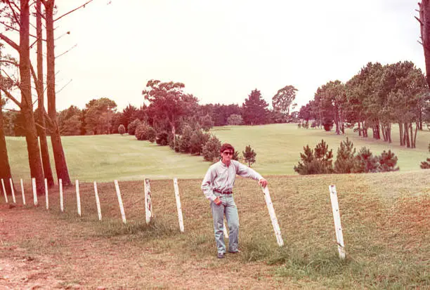 Vintage image of a young man standing by a fence in the field.
