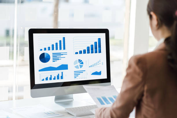 istock Young attractive Asian woman holding chart paper checking financial data in computer, looking to monitor, rear view shot. 1391967143