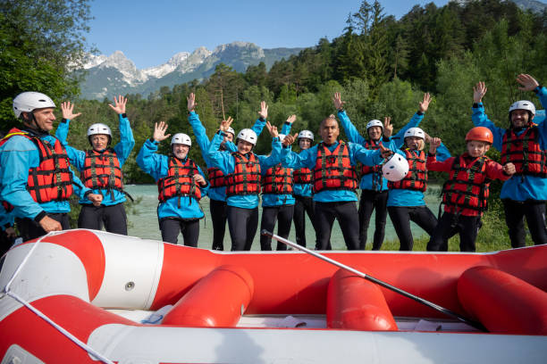 Multiracial team standing with raised hands near inflatable raft Wide shot of multiracial team standing with raised hands near inflatable raft. Smiling people looking for adrenaline experience in nature. Rafting in wild mountain Soca river, Slovenia. primorska white sport nature stock pictures, royalty-free photos & images