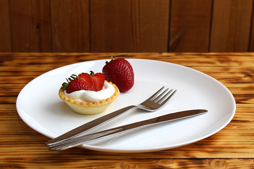 Tartlets with cream and strawberries are on a plate.