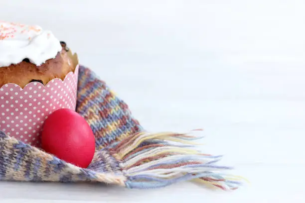 a red chicken egg and a festive cupcake are wrapped in a knitted scarf