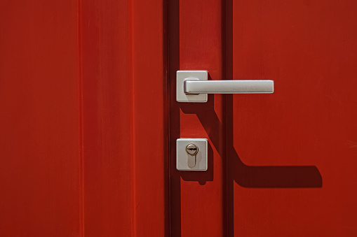 Red colored door with handle and lock close-up in a natural sunlight