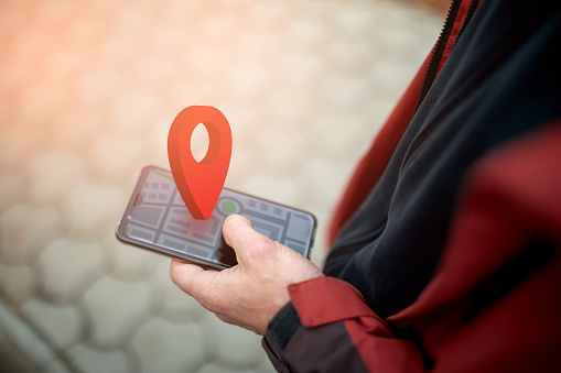 Online navigation and GPS. Geolocation sign above smartphone screen with abstract online map. Close-up of man's hand using a smartphone on street