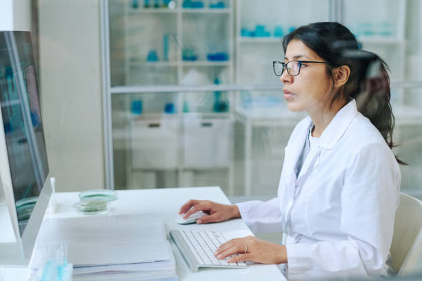 istock Young pretty female scientist in whitecoat and eyeglasses using computer 1391972426