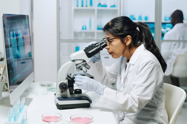 istock Side view of female biochemist looking in microscope while studying virus 1391972473